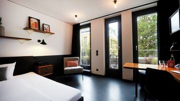 A modern hotel room with a bed, a desk, a chair, and a balcony with a view.