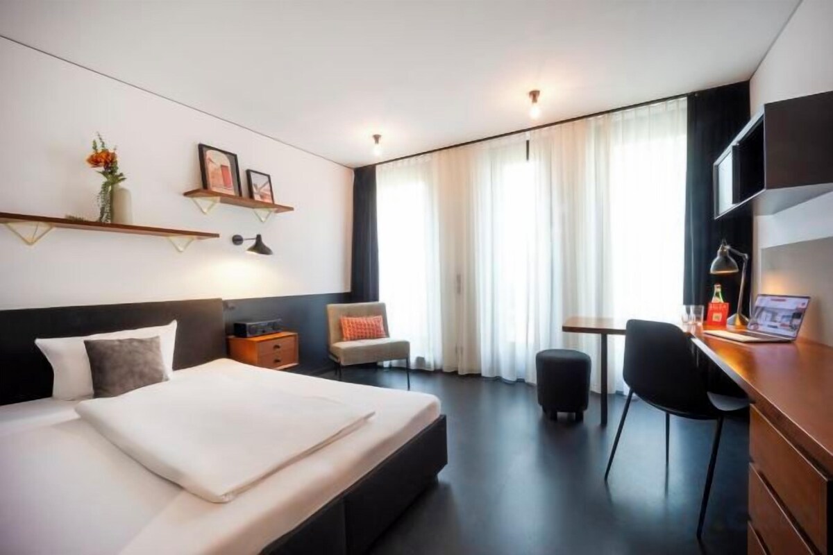 A modern hotel room with a large bed, a desk, a chair, and a TV.