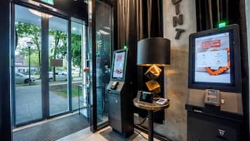 A modern hotel entrance with a check-in kiosk, a digital display, and a reception desk.