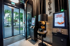 A modern hotel entrance with a check-in kiosk, a digital display, and a reception desk. - Brera Serviced Apartments Schwabing (Munich)