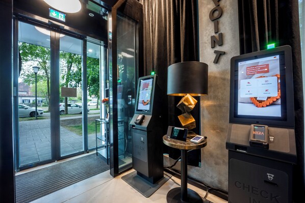 A modern hotel entrance with a check-in kiosk, a digital display, and a reception desk. - Brera Serviced Apartments Schwabing (Munich)