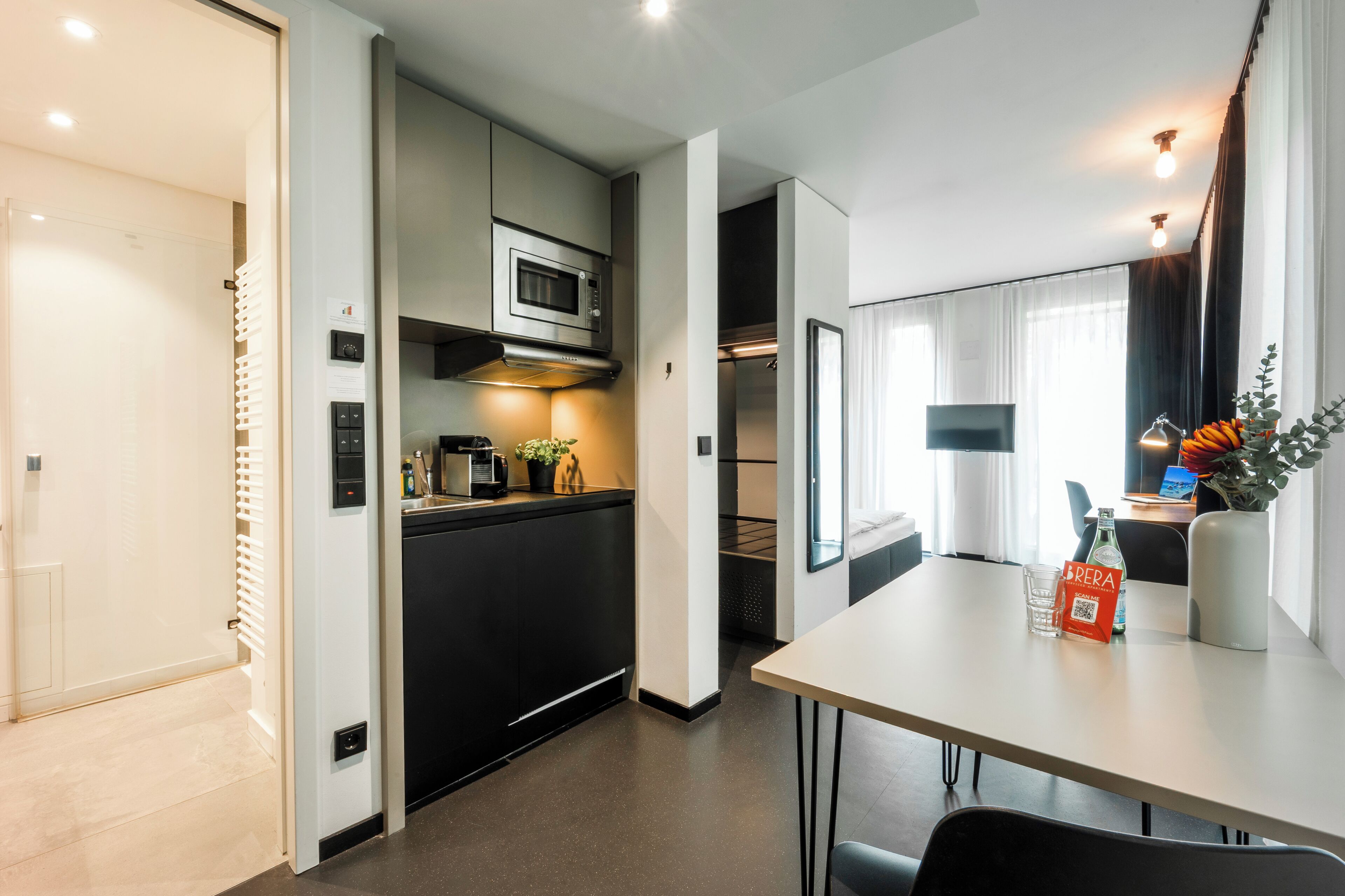 A modern hotel room with a kitchenette, a dining area, and a bed.