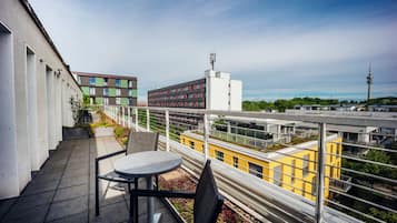 Un balcón con mesa y sillas, con vistas a un paisaje urbano con edificios modernos y una torre.
