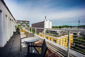 Un balcón con mesa y sillas, con vistas a un paisaje urbano con edificios modernos y una torre.
