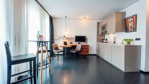 A modern kitchen with a flat-screen TV, a dining area with a table and chairs, and a large window with curtains. - Brera Serviced Apartments Schwabing (Munich)