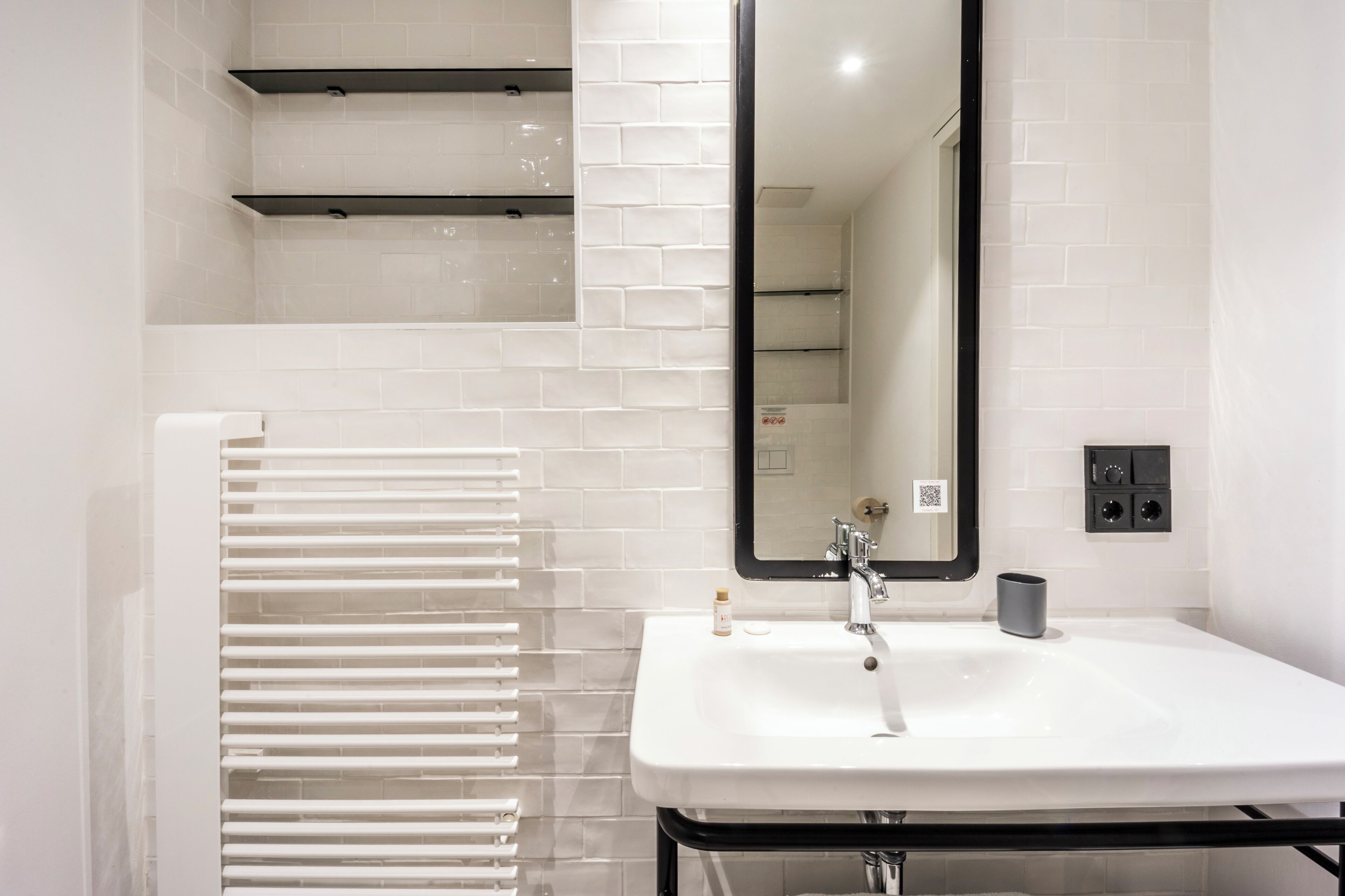 Un baño moderno con un lavamanos blanco, un espejo y un perchero para toallas.