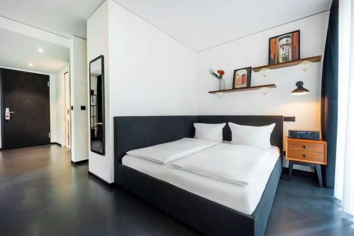 Una habitación de hotel moderna con una cama grande, una mesita de noche y un espejo.