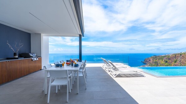 A modern outdoor dining area with a view of the ocean and a pool.