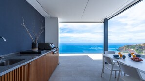 A modern kitchen with a view of the ocean, a dining area with a table and chairs, and a large window.