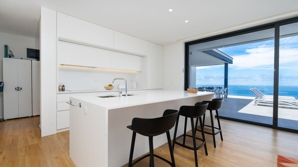 A modern kitchen with a large island, bar stools, and a view of the ocean.