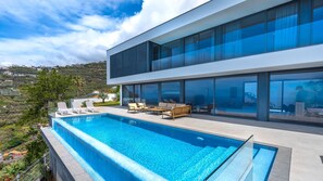 Une maison moderne dotée d’un grand balcon en verre, d’une piscine et de mobilier d’extérieur.