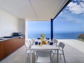 A dining area with a table set for four, overlooking a scenic ocean view. - Heaven's Nest by LovelyStay (Ponta do Sol)