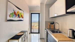 Une cuisine moderne avec vue sur la mer, un coin repas avec une table noire et un tableau abstrait aux couleurs vives accroché au mur.