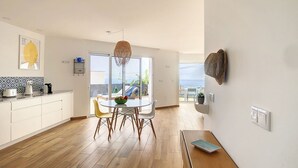 Une cuisine moderne avec des meubles blancs, une table à manger avec des chaises et une vue sur l’extérieur.