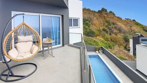 Un balcon avec un fauteuil suspendu, une petite table avec un verre et une piscine.