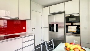 A modern kitchen with a stainless steel refrigerator, oven, and a red backsplash.
