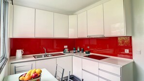 Una cocina moderna con armarios blancos, un salpicadero rojo y un bol con fruta sobre la encimera.