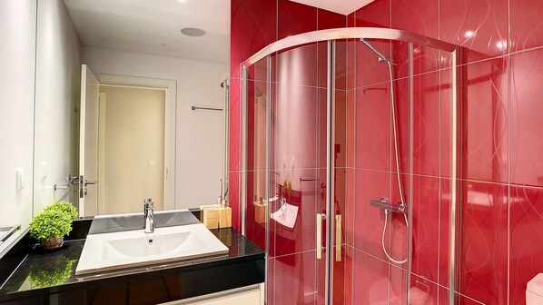 Un baño moderno con cabina de ducha de vidrio, lavamanos con encimera negra y un espejo.