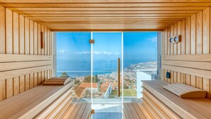 A sauna with wooden walls and benches, a large glass window, and a view of a coastal city.