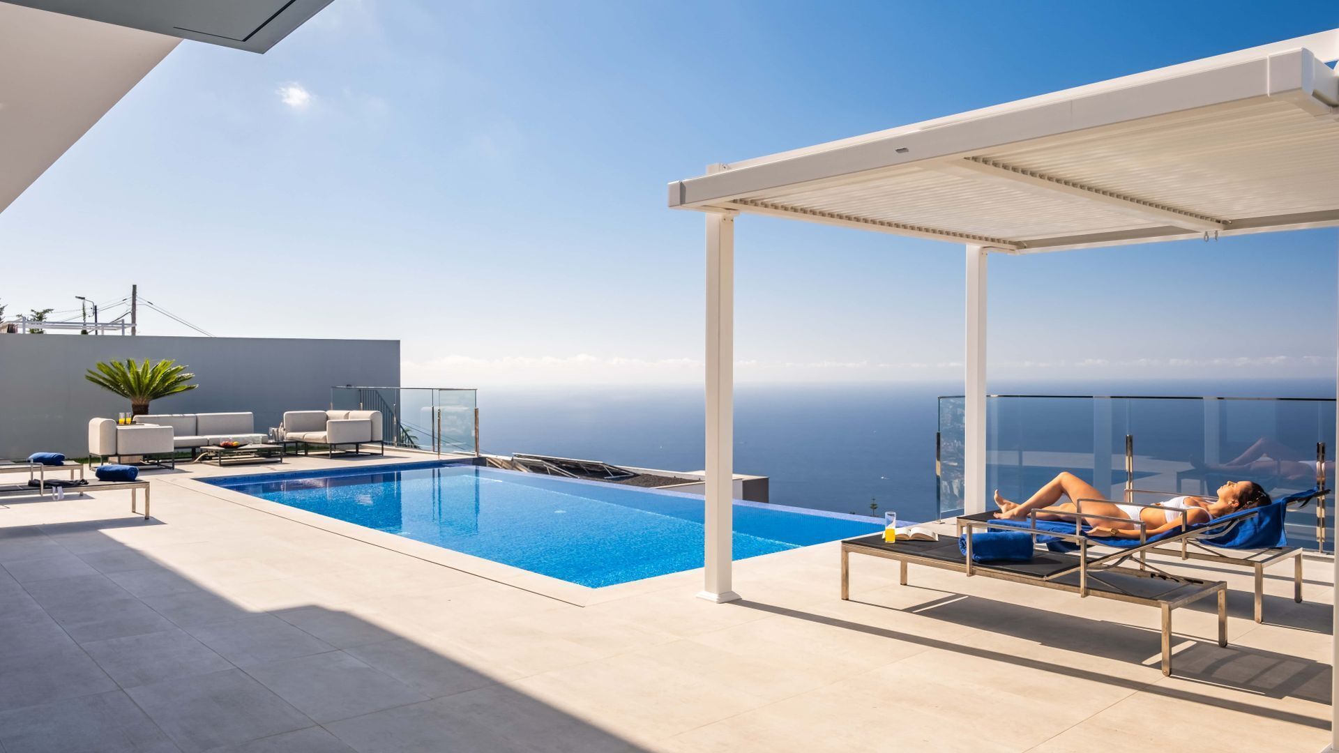 Ein Dachpool mit unendlicher Optik und freiem Blick auf den Horizont, ein überdachter Sitzbereich und eine moderne Lounge mit Topfpflanze.
