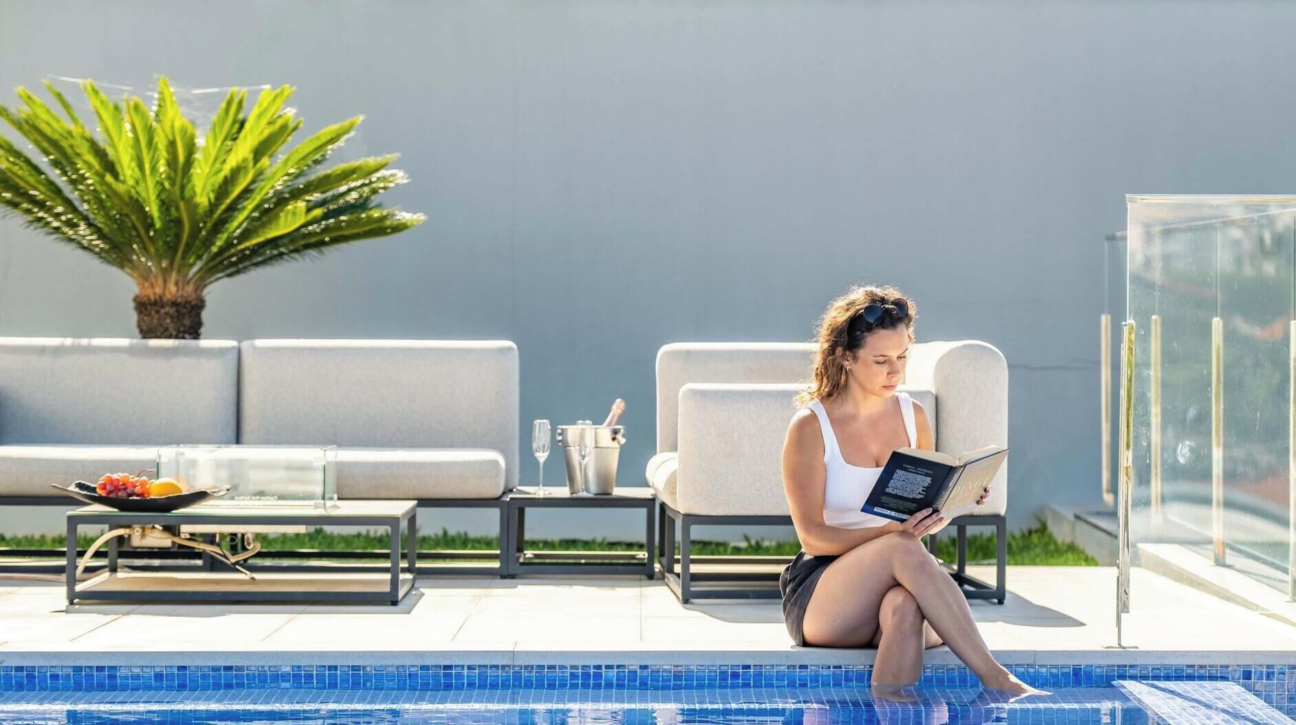 Zona junto a la piscina con sillones de descanso, una mesa con frutero y una planta en maceta.