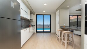 A modern kitchen with a large sliding glass door leading to a pool. - Evoque Villa by LovelyStay (Arco Da Calheta)