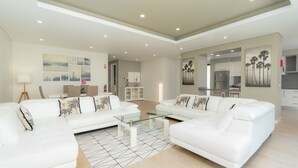 A modern living room with white sofas, a glass coffee table, and a dining area with a white cabinet. - Evoque Villa by LovelyStay (Arco Da Calheta)