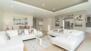 A modern living room with white sofas, a glass coffee table, and a dining area with a white cabinet. - Evoque Villa by LovelyStay (Arco Da Calheta)