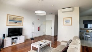 Una sala de estar moderna con un televisor de pantalla plana, un sofá blanco, una mesa de centro y un comedor con mesa y sillas.