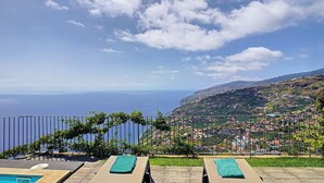Vista de la piscina con sillones de descanso, cielo despejado y una lejana vista de un pueblo costero.
