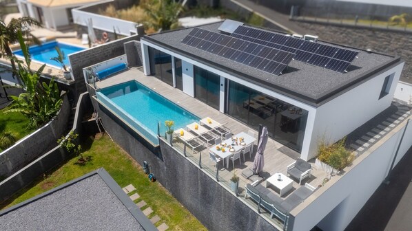 Une maison moderne dotée d’une piscine, de panneaux solaires et de mobilier d ’extérieur.