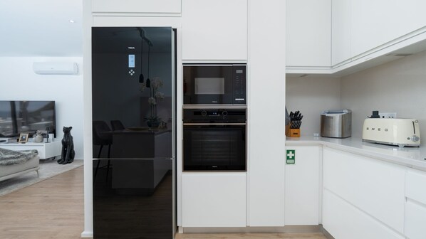 A modern kitchen with built-in appliances, a dining area with a TV, and a living room with a sofa and a cat statue. - Villa Lilian - Three Bedroom House, Sleeps 6 (Arco Da Calheta)