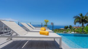 Un espace aménagé au bord de la piscine, avec des chaises longues et une vue sur l’océan.
