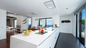 A modern kitchen with a large island, a dining area with a view, and a living space with a sofa and a fireplace. - Unmei Villa by LovelyStay (Caniço)