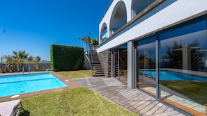Una casa moderna con piscina, un pontile in legno e una scala in pietra che conduce a una porta in vetro.