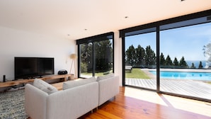A modern living room with a large TV, comfortable seating, and a view of a swimming pool. - Unmei Villa by LovelyStay (Caniço)