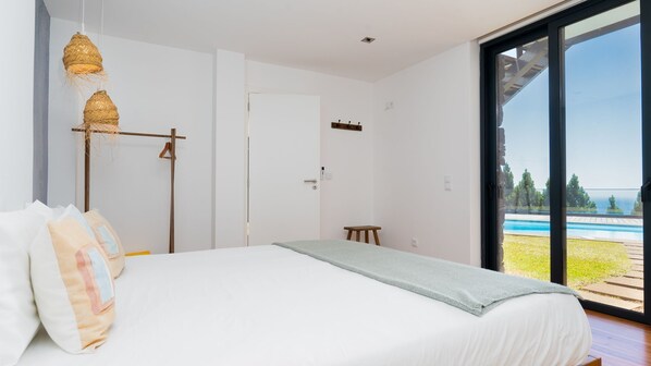 A bedroom with a large bed, a hanging light fixture, a door, and a view of a swimming pool.