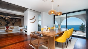 Zona pranzo moderna con tavolo in legno, sedie gialle e vista sul mare.