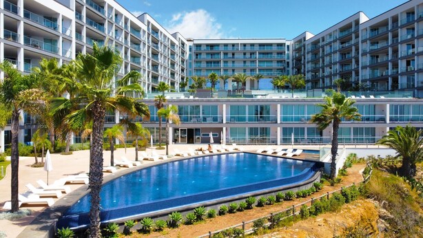 Un hotel moderno con una piscina grande, varios balcones y palmeras.