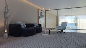 A modern living room with a dark blue sofa, a glass coffee table, and a view of the ocean through large windows.