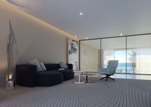 A modern living room with a dark blue sofa, a glass coffee table, and a view of the ocean through large windows.