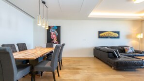 Ein modernes Wohnzimmer mit einem Holzesstisch, grau gepolsterten Stühlen, einem schwarzen Ledersofa und einem Baumgemälde an der Wand.