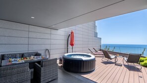 A modern outdoor deck with a hot tub, lounge chairs, and a dining area with a view of the ocean.