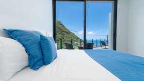 A bedroom with a bed, a view of a mountainous landscape, and a balcony with a chair and a wicker basket. - Villa Stella by LovelyStay (Arco Da Calheta)