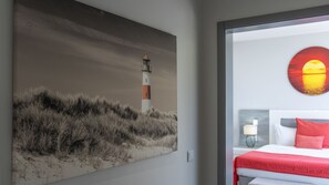 A room with a large painting of a lighthouse, a bed with a red blanket, and a sunset painting on the wall. - Villa Stella by LovelyStay (Arco Da Calheta)