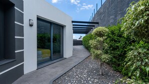 A modern building with a glass door, a pathway, and a hedge. - Villa Stella by LovelyStay (Arco Da Calheta)