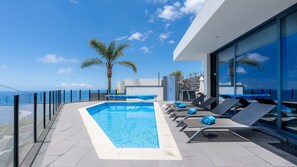 A rooftop pool with clear blue water, surrounded by lounge chairs and a glass balustrade. - Villa Stella by LovelyStay (Arco Da Calheta)
