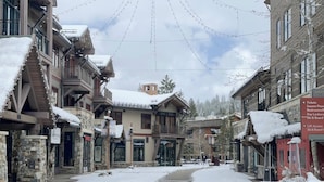 Een sneeuwbedekte straat met gebouwen aan weerszijden, waaronder een stenen gebouw met een bord voor een restaurant en een gebouw met een bord voor een skilift.