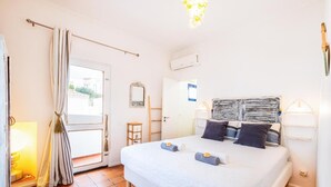A bedroom with a bed, curtains, a lamp, an air conditioning unit, and a door. - Fisherman's cottage a few steps from the beach (Olhos de Água)
