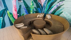 A circular wicker sofa with cushions, set against a wall with a tropical leaf mural. - Villa Elizabeth Beach Resort (Lucena)